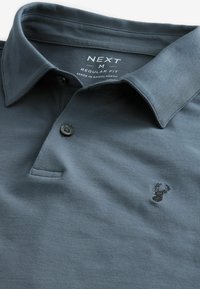 Polo de color gris oscuro, hecho de algodón, con cuello abotonado y un pequeño logotipo bordado en el lado izquierdo del pecho. Diseño de ajuste regular.