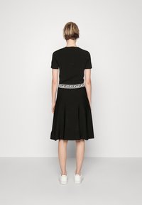 Abito nero con corpetto aderente e gonna svasata. Presenta una cintura bianca con motivo. La modella indossa sneakers bianche. La vista posteriore mostra maniche corte.