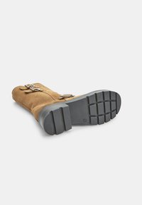 Pruunist sametist valmistatud ankle boots, millel on tekstureeritud pealis ja must kummist talla. Omab kahte hõbedast kinnitust ja robustset mustrit tallal.