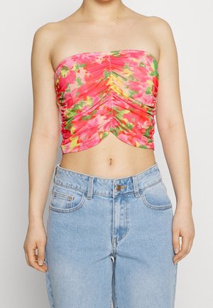 Trägersloses Oberteil im lebhaften pinken und grünen Blumendruck, mit gerafften Stoffdetails; kombiniert mit hochgeschnittenen hellblauen Jeans.