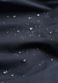 Voděodolná černá tkanina s hladkým povrchem, na kterém jsou rozptýlené kapky vody, což zdůrazňuje její voděodolné vlastnosti.