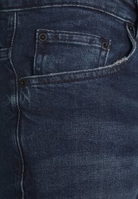 Mörkblå denimjeans med en subtil urtvättad effekt, med en liten framficka och svart metallspänne för stängning.
