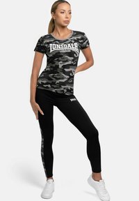 Camo t-shirt in black and gray with a white logo, paired with black leggings featuring a camo stripe, worn with white sneakers.
