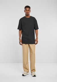 Schwarz kurzärmliges T-Shirt mit lockerer Passform, kombiniert mit beigen weiten Hosen und beigen Sneakers, vor einem hellen Hintergrund stehend.