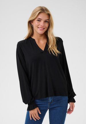 Black long-sleeve top with a V-neckline, elasticized cuffs, and soft texture. Paired with fitted blue denim jeans.