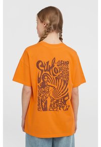 Oranžové bavlněné tričko s velkým hnědým grafickým designem na zadní straně, jehož součástí je postava a vířící text, volný střih, krátké rukávy.