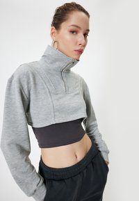 Grijze cropped sweatpants met een hoge kraag en een halve rits, van structuurstof, gecombineerd met een donkergrijze crop top en zwarte jogpants met trekkoord.
