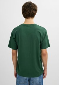 Camiseta de algodón verde con mangas cortas y cuello redondo, que presenta un diseño liso y un corte holgado. La vista posterior muestra una textura suave.