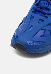 Blauwe sportschoen met een gestructureerd mesh bovendeel, glanzende accenten en een zwarte rubberen buitenzool. Voorzien van versterkte stiksels en logo's.