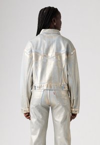 Metallic ljusblå denimjacka med klassisk krage, ryggdetalj och knappade ärmar. Har sydda detaljer och en skräddarsydd passform.