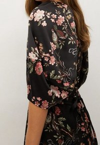Vestido de satén negro con patrones florales en rosa y verde, con mangas cortas y un lazo en la cintura, que resalta su delicado diseño.