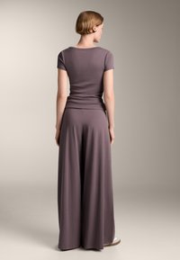 Top gri cu maneci scurte asociat cu pantaloni gri, largi și fluidi. Ambele au o textură netedă și o siluetă ajustată la talie.