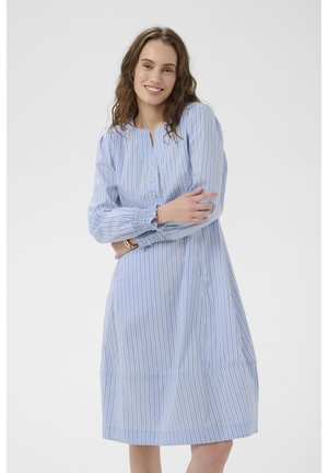 Mėlyna dryžuota suknelė su ilgomis rankovėmis, priekyje su sagomis ir surinktais rankogaliais. A linijos siluetas su šiek tiek praplatėjusia apačia, pagaminta iš lengvos medžiagos.