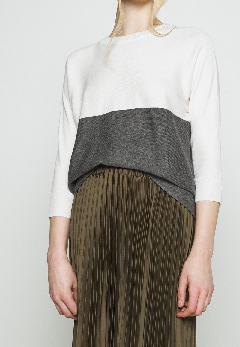 Maglione leggero con una parte superiore crema e una striscia orizzontale grigia scura. Abbinato a una gonna plissettata verde oliva, che mette in risalto una texture liscia e un design a strati.