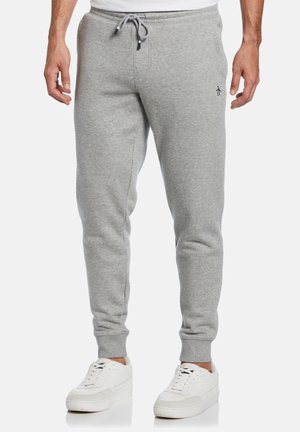 Grijze joggingbroek gemaakt van een zachte stof, met een tailleband met trekkoord, taps toelopende benen en een klein logo bij de heup. Gepaard met witte sneakers.