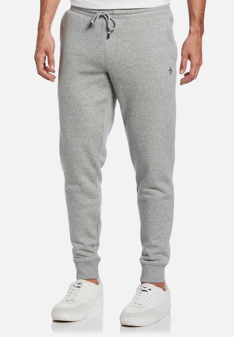 Grijze joggingbroek gemaakt van een zachte stof, met een tailleband met trekkoord, taps toelopende benen en een klein logo bij de heup. Gepaard met witte sneakers.