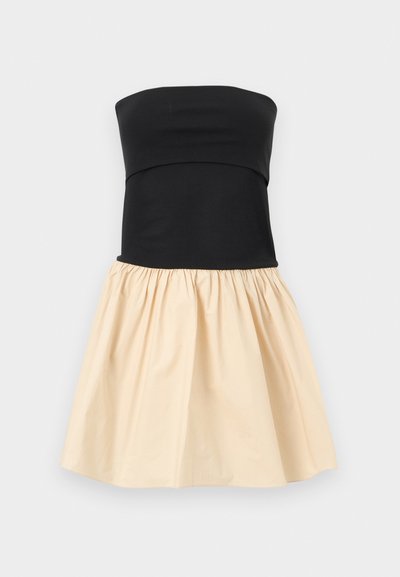 Αμάνικο φόρεμα με εφαρμοστό μαύρο κορσέ και σιφόν μπεζ φούστα, φουσκωτή και με πιέτες, που τελειώνει πάνω από το γόνατο, σε ανοιχτό γκρι φόντο.