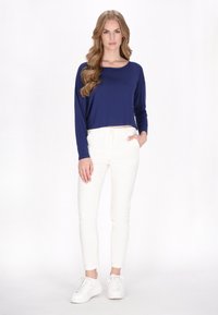 Tengerészeti hosszú ujjú crop top, ami passzol a testhez álló fehér nadrághoz és fehér sportcipőhöz, sima felszínt és egyszerű dizájnt mutatva.