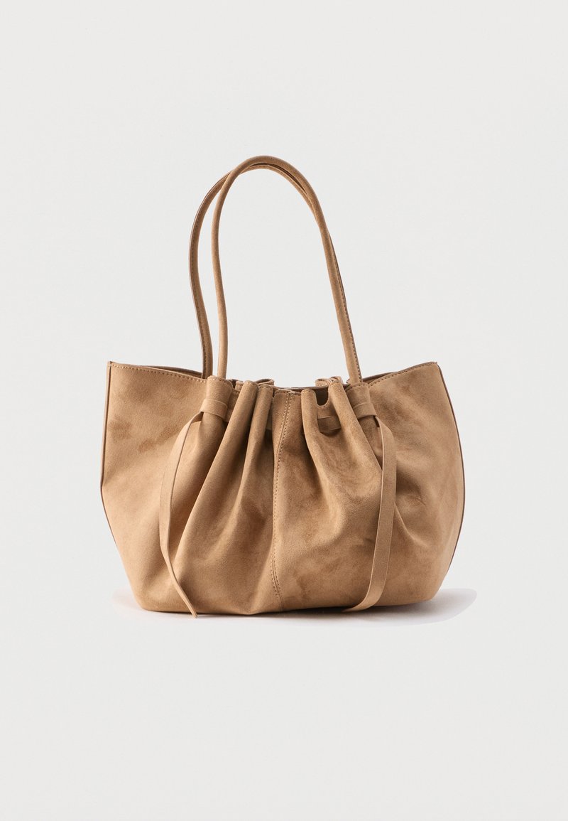 Τσάντα tote από καφέ καστόρι με λεπτομέρειες ραμμένες στην κορυφή και δύο μακριές λαβές σε απλό λευκό φόντο.