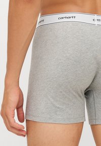 Boxeri gri din bumbac cu un elastic alb ce poartă logo-ul "Carhartt" în negru. Materialul este moale și ușor elastic.