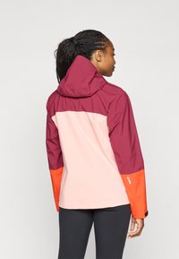 Veste imperméable en maron, rose et orange. Comprend une capuche, des couleurs de manches contrastées et des poignets réglables. Légère, texture lisse.