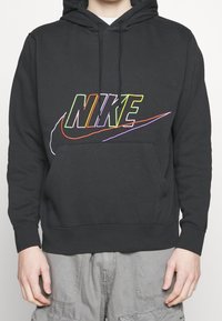 Black hoodie made from cotton blend, featuring multicolored embroidered "NIKE" logo and a front pocket. Includes a drawstring hood.