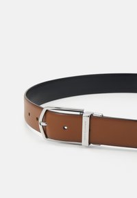 Cintura in pelle marrone con una superficie liscia, dotata di una fibbia in metallo argentato e un interno nero. Include più fori di regolazione.