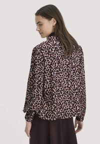 Langärmlige Bluse aus pinkem Stoff mit Leopardenmuster. Sie hat einen hohen Ausschnitt und eine entspannte Passform mit gerafften Ärmeln.