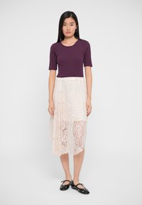 Top violet ajustat cu mânecă scurtă, asociat cu o fustă midi din dantelă crem, cu modele florale și un overlay transparent. Pantofi plata negri.