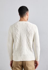 Cremfarbener Grobstrickpullover mit gerippten Bündchen und Saum, der mit Rauten- und vertikalen Mustern gestaltet ist, aus strukturiertem Garn gefertigt.