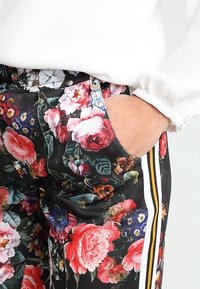 Svarta blommiga byxor har livfulla rosa, röda och blå blommor, vita och gula sidostråk, samt en fickdetalj i midjan.