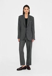 Grijs krijtstreeppak met een getailleerde blazer en rechte broekspijpen, gecombineerd met een zwart topje en donkere loafers. Soepele stoftextuur.