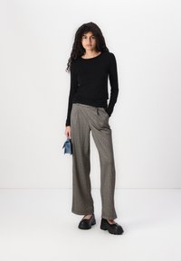Fekete, hosszú ujjas felső, világos, texturált, átlátszó anyagból. Szürke és barna kockás, bőszárú nadrág, fekete platform cipővel és kék clutch táskával párosítva.