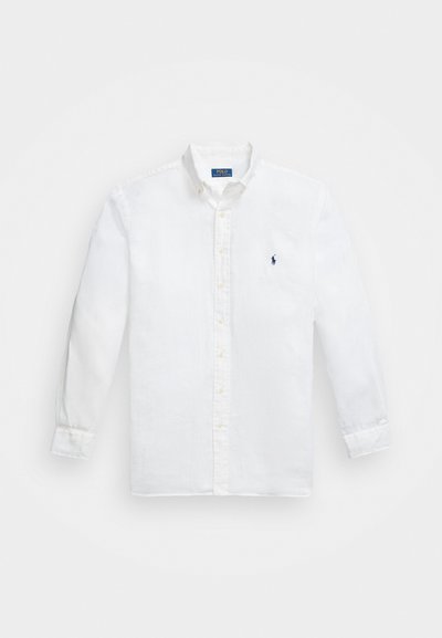Λευκό πουκάμισο με μακριά μανίκια και κουμπιά από ελαφρύ ύφασμα, με κλασικό γιακά, μπροστινά κουμπιά και ένα μικρό ναυτικό λογότυπο στο στήθος.