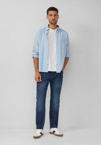 Jasnoniebieska koszula w kratę noszona na białym t-shircie, w połączeniu z granatowymi dżinsami i białymi trampkami z szarymi akcentami. Swobodny fason, wywinięte rękawy.