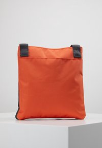 Oranžová taška z látky s černými akcenty, čtvercový tvar, zesílené úchyty, textura se zdá hladká, žádné viditelné kovové prvky nebo vzory.