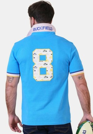 Homme portant un maillot de rugby bleu vif avec le numéro 8 et de petites impressions de voitures au dos, tenant un ballon de rugby dans la main droite.