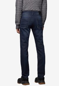 Jeans in denim blu scuro con vestibilità slim, caratterizzati da tasche posteriori e un leggero sbiadimento sulle gambe. Abbinati a un maglione lavorato a maglia con motivo.