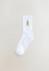 White cotton socks with ribbed texture, featuring an embroidered yellow Fanta bottle graphic on the side.