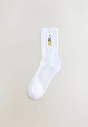White cotton socks with ribbed texture, featuring an embroidered yellow Fanta bottle graphic on the side.