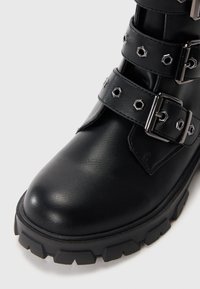 Čierna kožená členková topánka s okrúhlou špičkou, masívnou podrážkou a tromi nastaviteľnými páskami s hexagonálnymi cvokmi a striebornými kovovými detailmi.