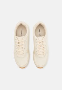 Krämfärgade sneakers med en slät syntetisk ovandel, rund tå och beige snörning. Har subtila sömmar och en gummisula.