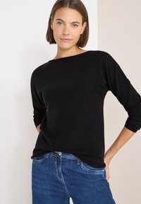 Maglione nero con scollatura rotonda, maniche lunghe e una texture morbida, abbinato a jeans di denim blu con una vestibilità classica e cinque tasche.