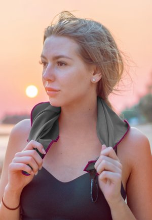 Grey cooling towel with purple trim draped around the neck, held by hands. Background features a sunset with soft pink and orange hues.