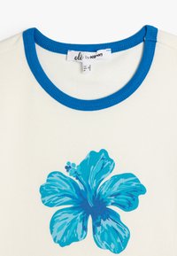 Top corto blanco de canalé con un diseño floral azul y un cuello redondo azul en contraste. La etiqueta dice "olé by keton" con detalles de tamaño.