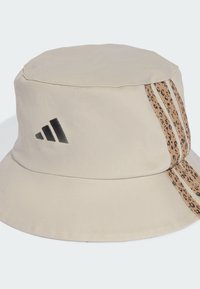 Beige bucket hat with a wide brim, featuring a textured fabric, black logo, and leopard print side stripes.