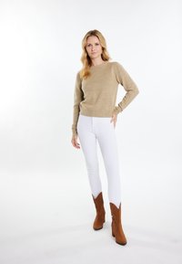 Hellbrauner Strickpullover mit langen Ärmeln, kombiniert mit weißen Slim-Fit-Jeans und braunen Wildleder-Stiefeletten mit dezenten Western-Details.