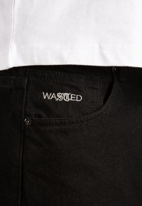 Jeans de mezclilla negra con una textura sutil, que presentan un logotipo bordado "WASTED" en el bolsillo trasero y un detalle de botón plateado.