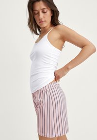 Top bianco abbinato a pantaloni corti a righe rosa con linee verticali blu navy. I pantaloni corti hanno una vita elastica per il comfort.
