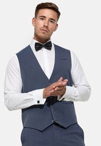 Gilet de costume bleu foncé en tissu texturé, avec un col en V, trois boutons et une poche unique. Assorti à une chemise blanche et un nœud papillon.